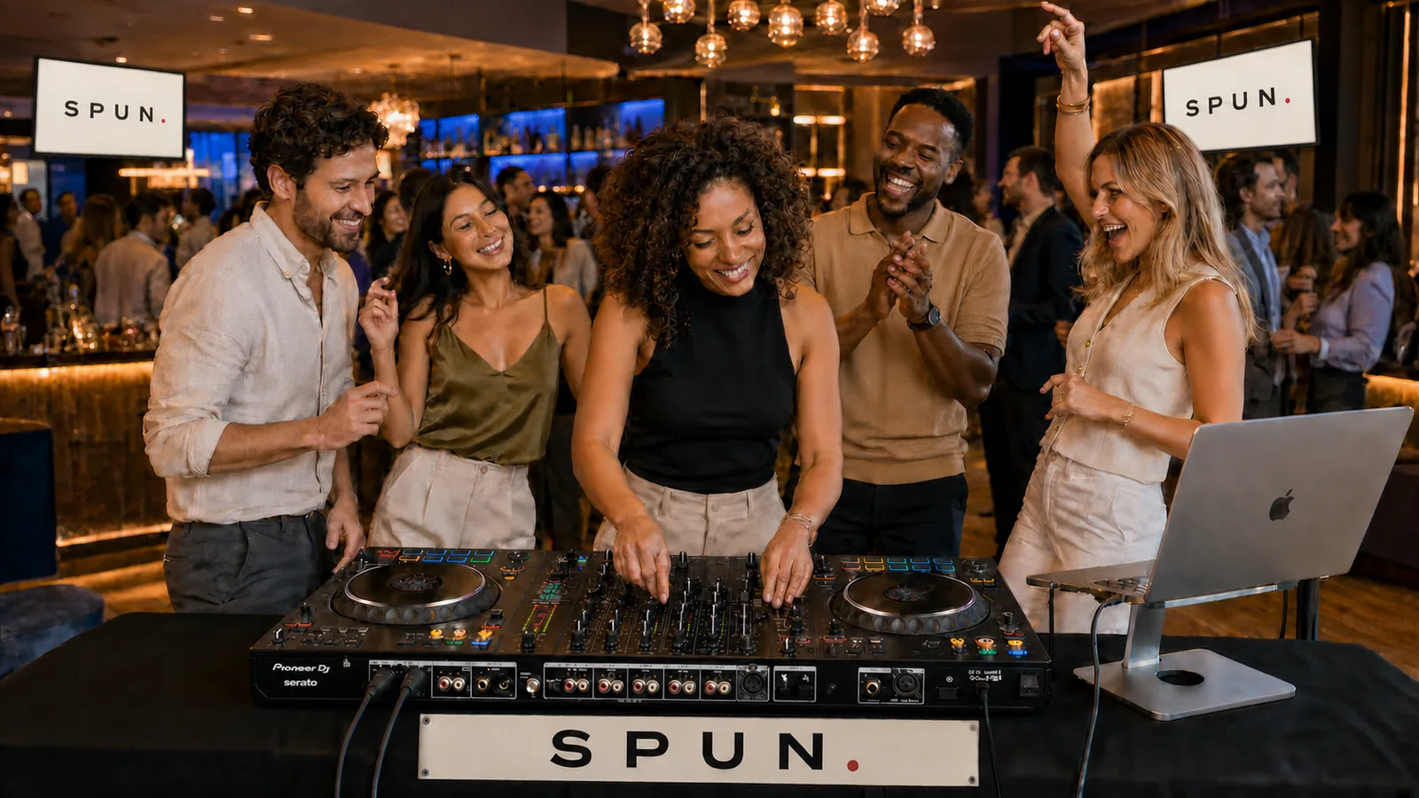A full group gathered around the decks together at a SPUN session, everyone laughing and celebrating